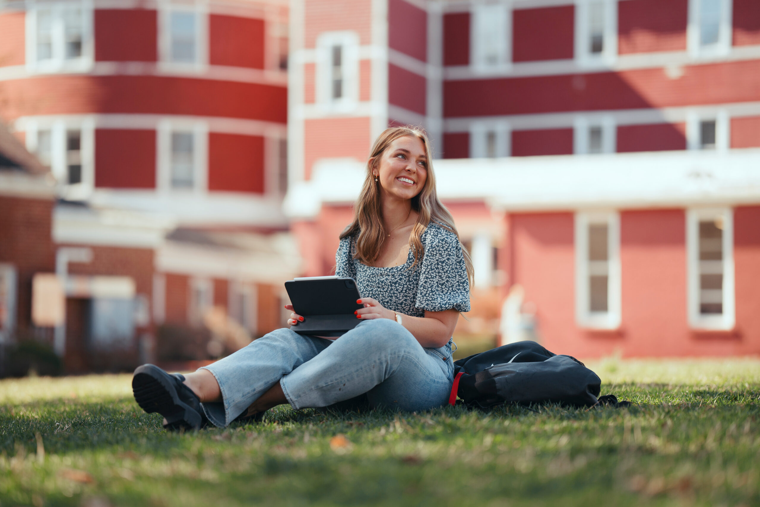 A Female student sitting on the grass with an iPad outside SVU Main Hall